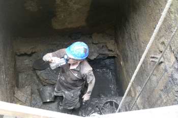 A man takes a drink break while working at the bottom of a muddy pit