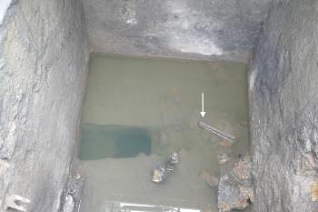 Water-filled pit with arrow pointing to object in the water