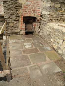 Flagstones on the floor of a stone building, with a fireplace set into an area of bricks at the back