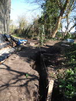A sunlight path is on the left, and there are trees in the background. A white string is stretched along the length of a trench on the right.
