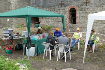A group of people sit between two gazebos, with the stone wall of a building in the background.