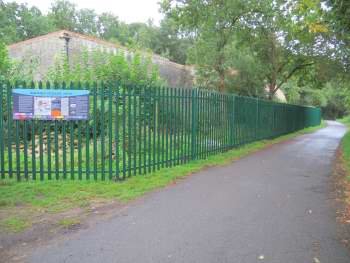 A green fence runs along the side of a path, with an interpretation board fixed to one end.