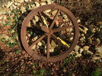 A reddish-coloured wheel rests against a stone stockpile.  The rim is conneceted to the stub axle by 7 spokes.