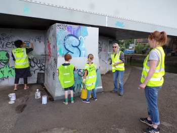 Five people in yellow hi-vi vests painting a wall